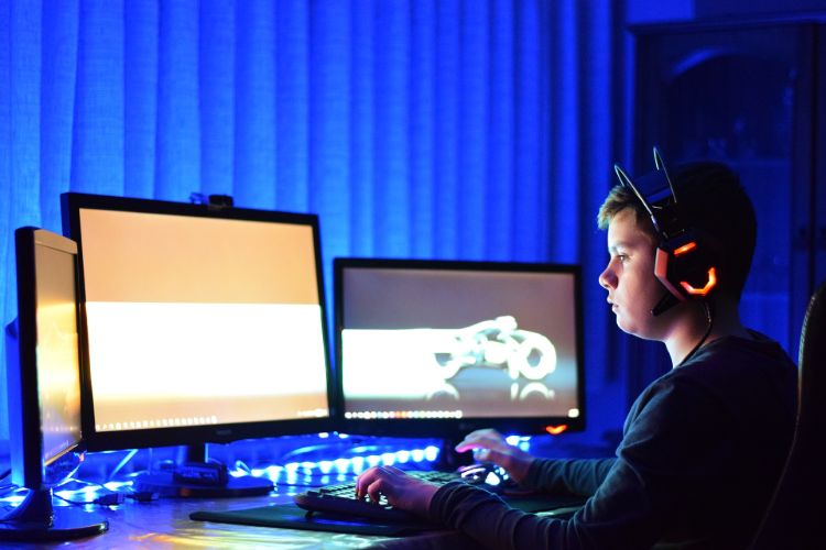 teenager zockt computerspiele mit kopfhörern auf drei monitoren