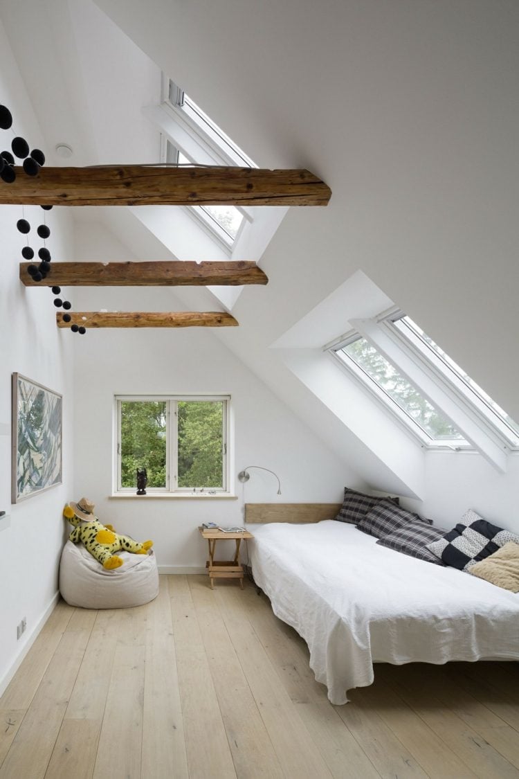 Hohes Dachzimmer in dreieckiger Form mit Dachfenstern, Balken und minimalistischer Einrichtung