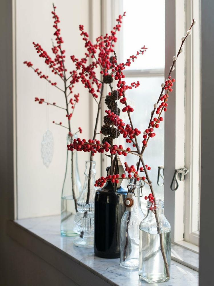 Idee mit Zweigen und roten Beeren in durchsichtigen Flaschen als Vasen