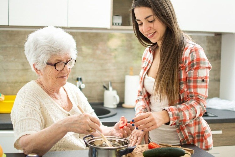 junge frau hilft alter dame mit alzheimer die zutaten beim kochen zu erkennen