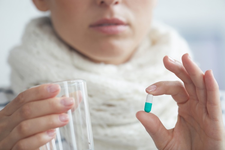 frau hält pille gegen influenza und wasserglas in der hand
