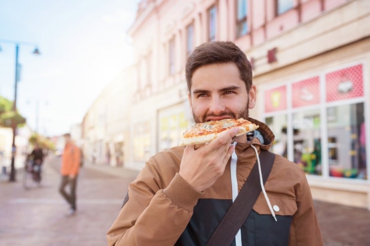 junger mann isst pizza auf der straße