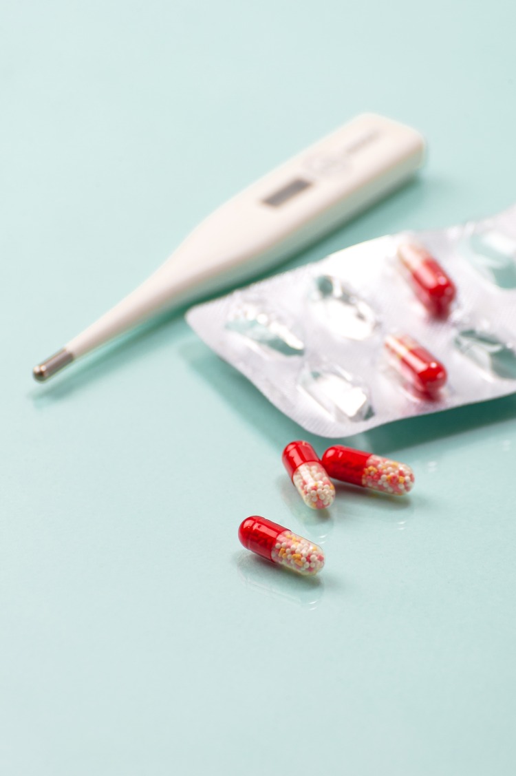 rotfarbene medikamente in verpackung und digitaler thermometer