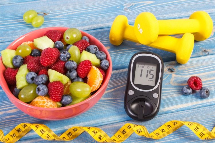 schüssel mit frischen fruchtstücken blutzuckermessgerät messband gewichte diabetes vorbeugungsmaßnahmen