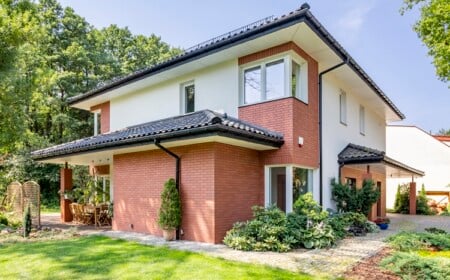 Rotes Backsteinhaus mit Terrasse und grünem Gras und Bäumen