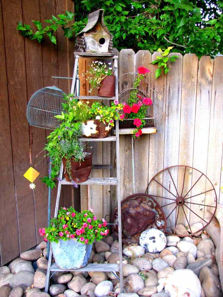 Vintage Gartendeko in Ecke vor dem Gartenzaun aus Leiter und Fahrradfelge