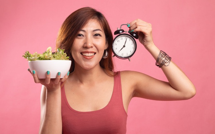 asiatin mit schüssel salat und wecker in der hand intermittierendes fasten