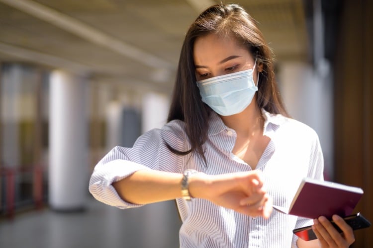 asiatische frau sieht auf ihre uhr mit mundschutz maske coronavirus update
