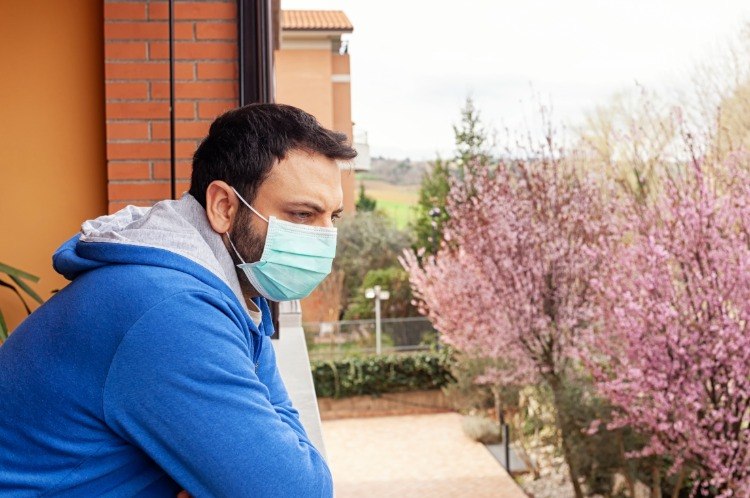 durchtrainierter mann mit schutzmaske am mund sieht aus dem balkon