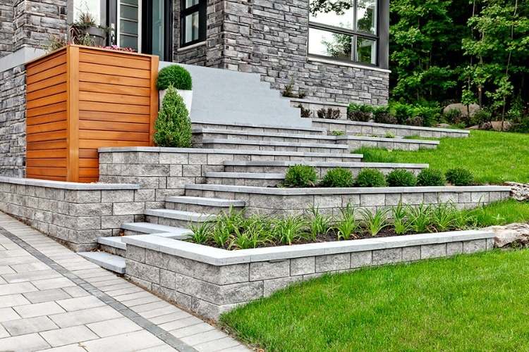 haus mit fassade aus grauem naturstein und terrasse mit stufen zum garten