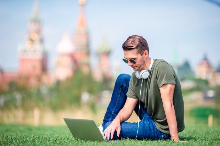 junger mann mit sonnenbrille kopfhörern und laptop sitzt auf einer wiese in moskau