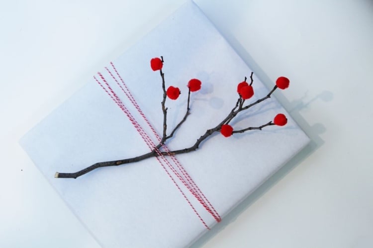 Schickes Geschenk mit weißer Verpackung und Zweig mit Beeren aus roten Bommeln