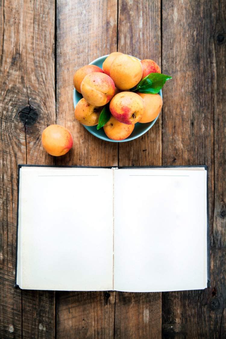 aprikosen in einer schüssel auf einem tisch mit leerem notizbuch