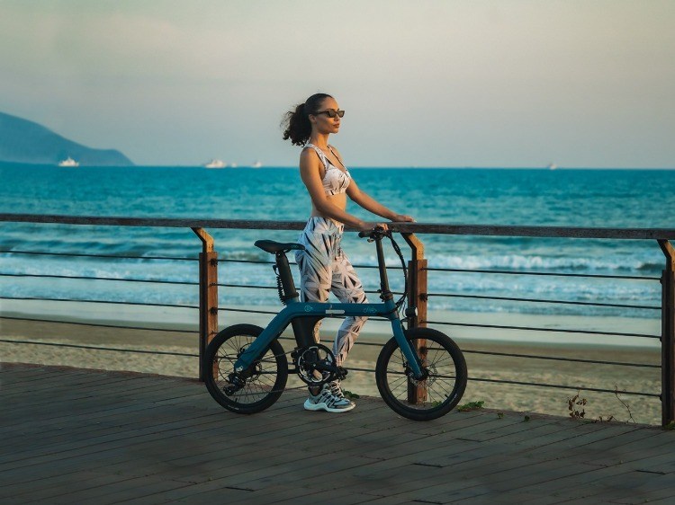 Woman with electric folding bike enjoys the sunset on the beach