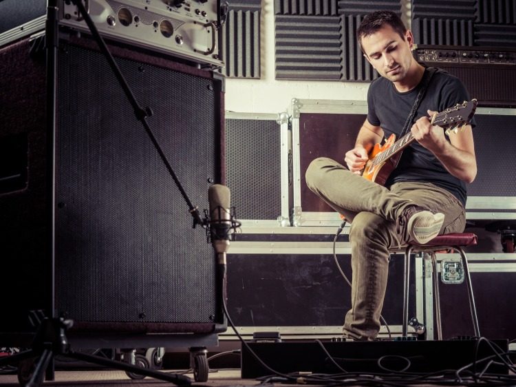 junger mann spielt gitarre bei aufnahmen in musikstudio mit gedämmter wannd