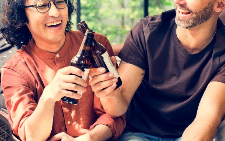 zwei lächelnde freunde beim biertrinken stoßen bierflaschen zum wohl