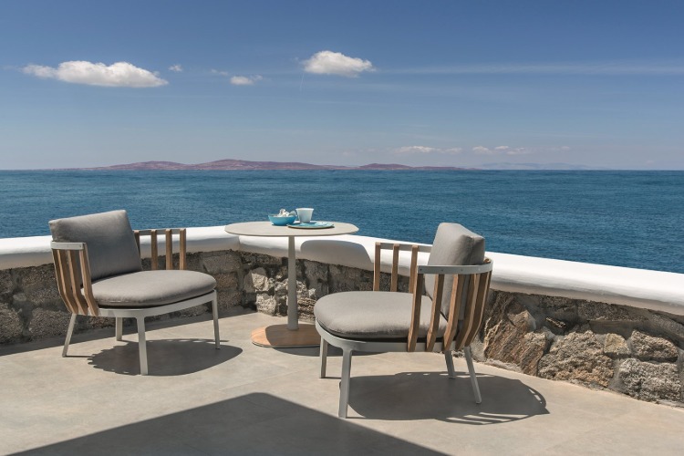 zwei sessel mit polsterung und runder tisch auf terrasse mit meeresblick auf insel