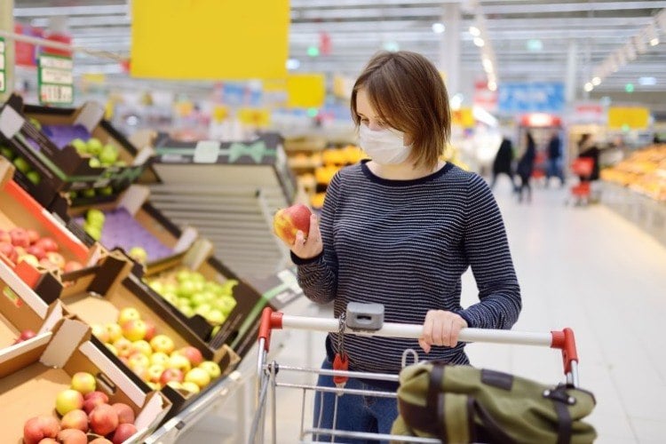 frau trägt schutzmaske während einkauf im supermarkt aufgrund von coronavirus