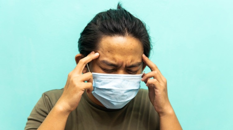 patient mit schutzmaske hält seinen kopf aufgrund von kopfschmerzen covid 19 symptome
