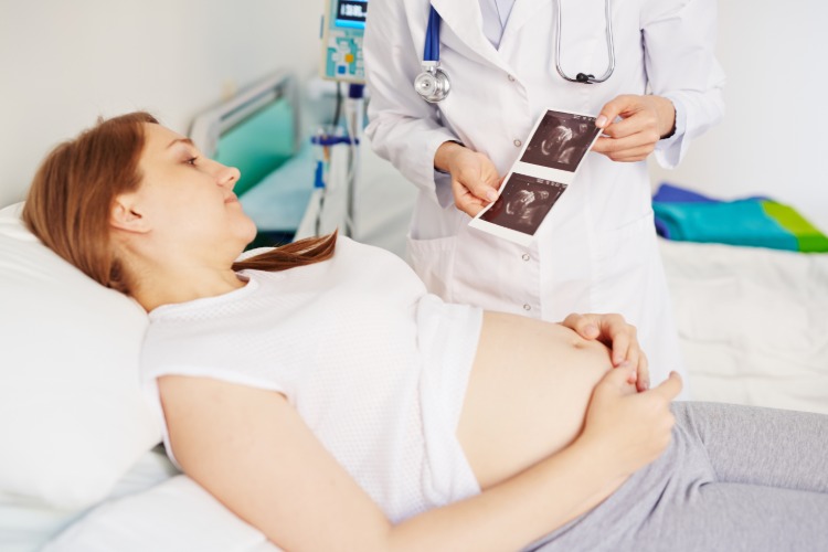 arzt zeigt aufnahme von fötus im krankenhaus an schwangere frau im bett
