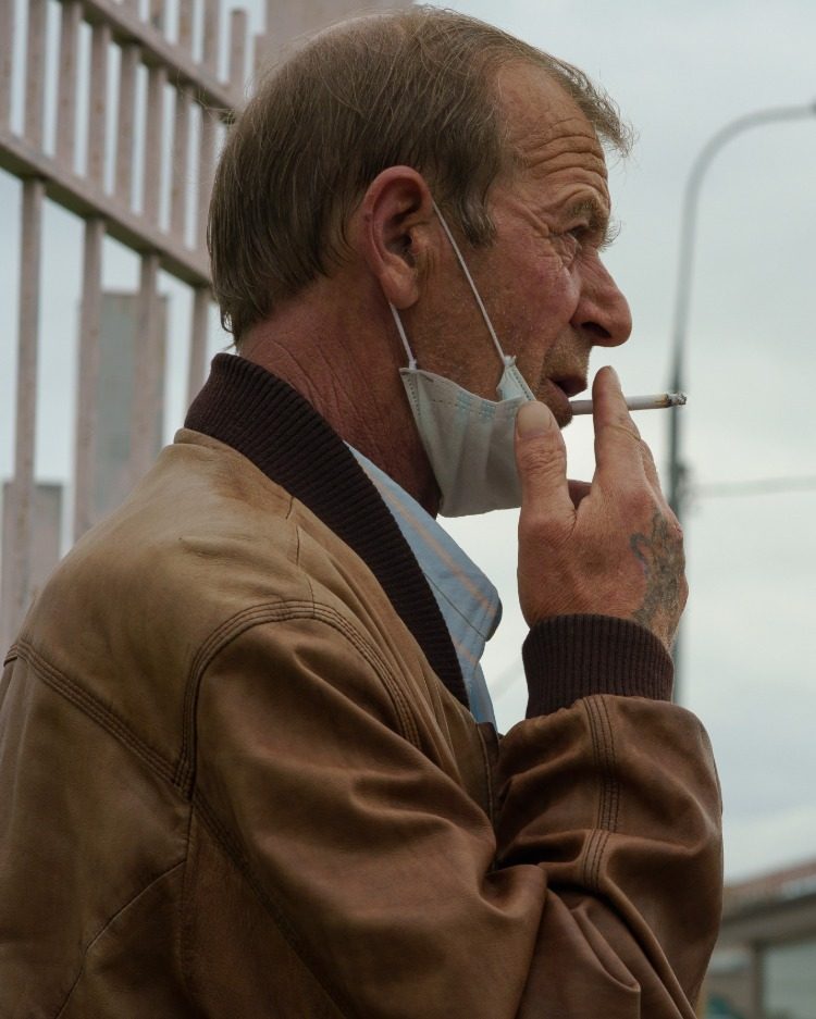 Elderly man smoking cigarette outdoors with protective mask removed