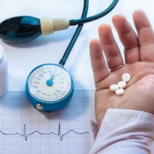blutdruckmedikamente in der hand halten neben blutdruckmessgerät mit kardiogramm