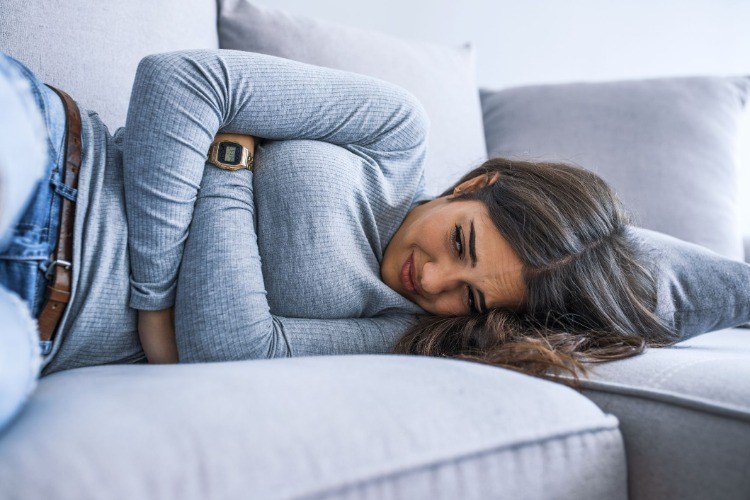 woman experiences salmonella symptoms such as vomiting and high fever and lies on the sofa with stomach cramps