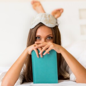 junge frau im bett mit schlafmaske und buch