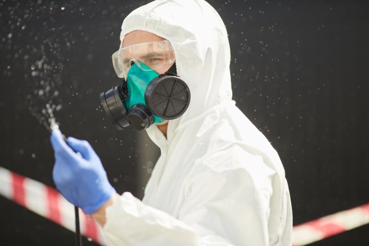 mann mit schutzkleidung bei desinfizierung während covid 19 pandemie