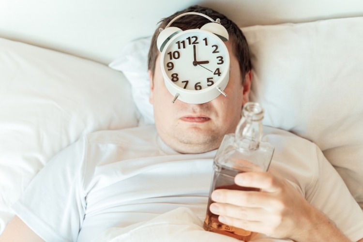 hungover man in bed with alarm clock and bottle of whiskey