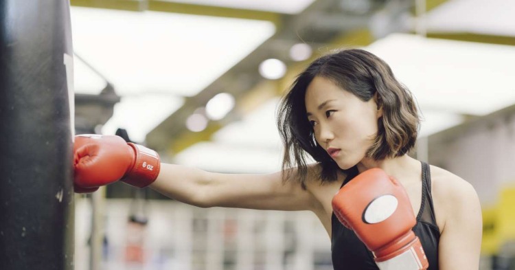 asiatische frau schlägt boxsack mit boxhandschuhen in einem sportraum