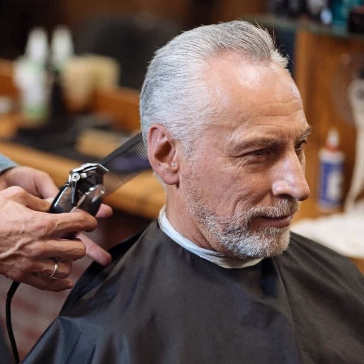 älterer mann mit weißen haaren im friseursalon lässt sich einen modernen haarschnitt machen