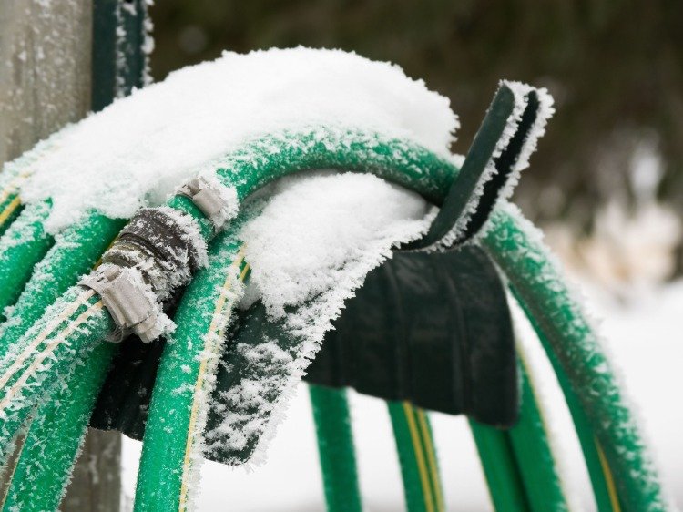 eingefrorener gartenschlauch mit schnee bedeckt im garten winterfest machen
