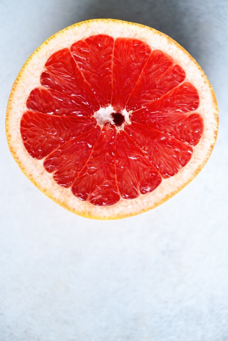 in hälfte geschnittene zitrusfrucht mit rotem fruchtfleisch auf grauem hintergrund