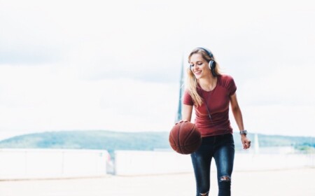 lächelnde junge frau mit kopfhörern und basketball als sportart zum gewichstverlust