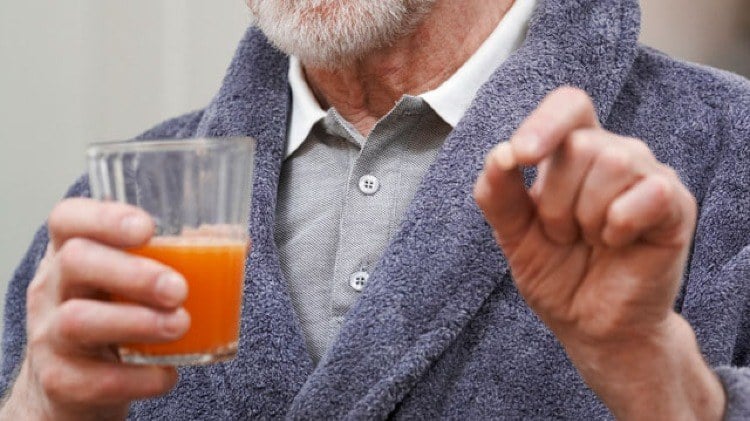 mann in hohem alter mit bademantel hält grapefruit und medikamente in der hand