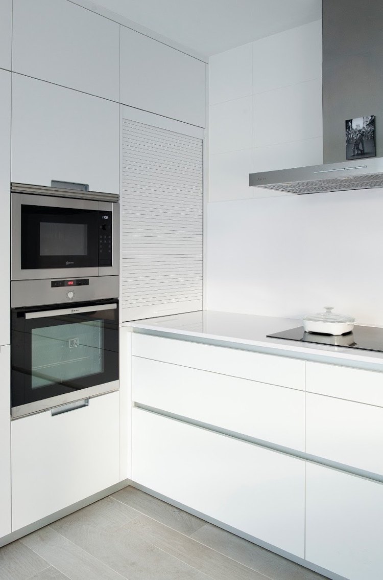 modern white kitchen with built-in appliances and roller shutter cabinet in the corner