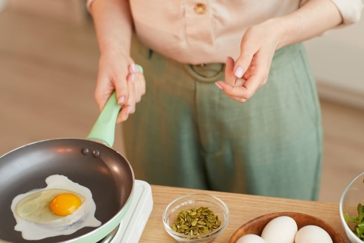 The woman cooks a fried egg for breakfast