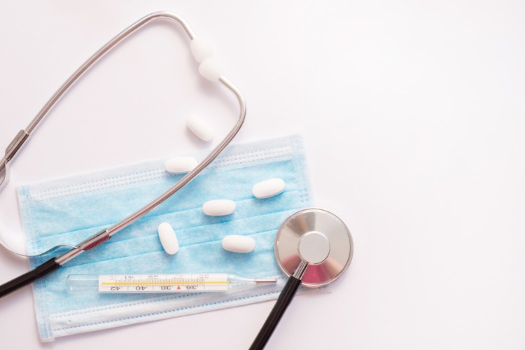aspirin tabletten auf schutzmaske neben thermometer und stetoskop