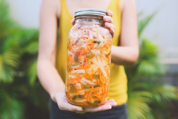 frau hält ein großes glas mit fermentiertem kimchi selber machen und gemüse einlegen
