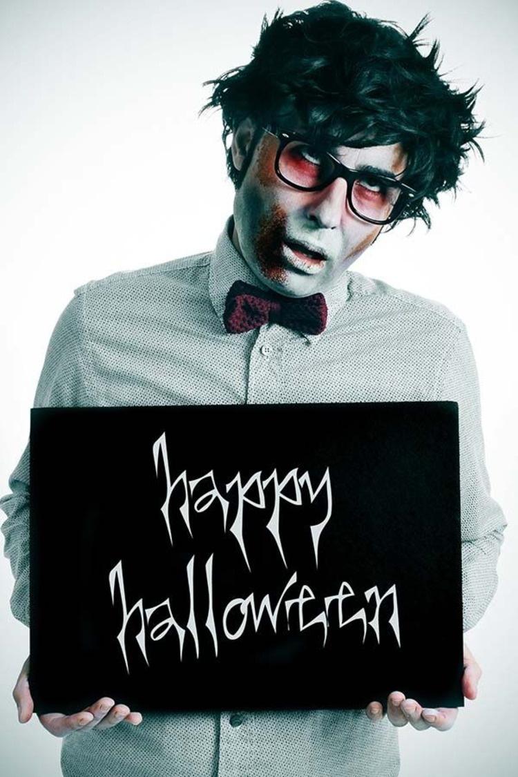 junger mann mit brillen zombie schminke hält happy halloween shild