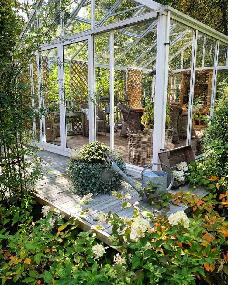 kaltwintergarten aus glas mit rattansesseln und rankhilfe für kletterpflanzen
