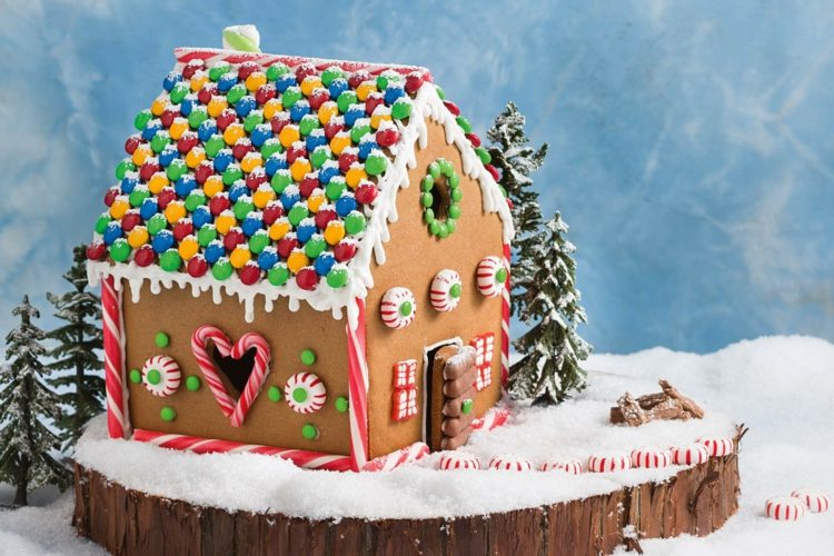 Schönes Lebkuchenhaus dekorieren mit bunten Smarties oder M&M's für das Dach und Zuckerstangen