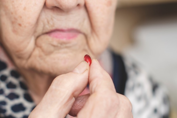 ältere frau hält eine rote pille in der hand vor der einnahme