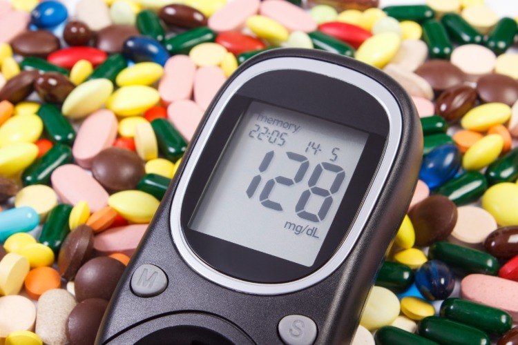 blutzuckermessgerät mit einem haufen von farbigen medikamenten gegen diabetes im hintergrund