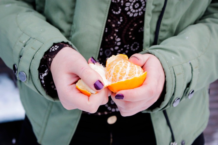 frau mit lilafarbener maniküre schält eine mandarine im freien bei kaltem wetter