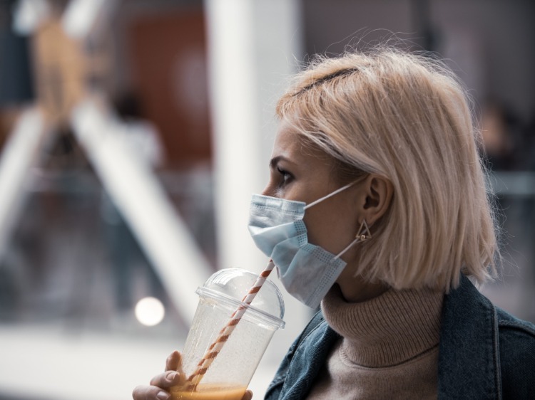 frau mit schutzmaske trinkt saft aus einem strohhalm während covid 19 pandemie