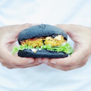 mann hält schwarzen vegan burger mit beiden händen