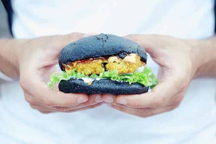 mann hält schwarzen vegan burger mit beiden händen