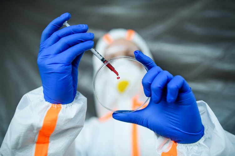 wissenschaftler mit schutzkleidung hält reagenzglas und blutprobe von covid 19 patienten zur analyse